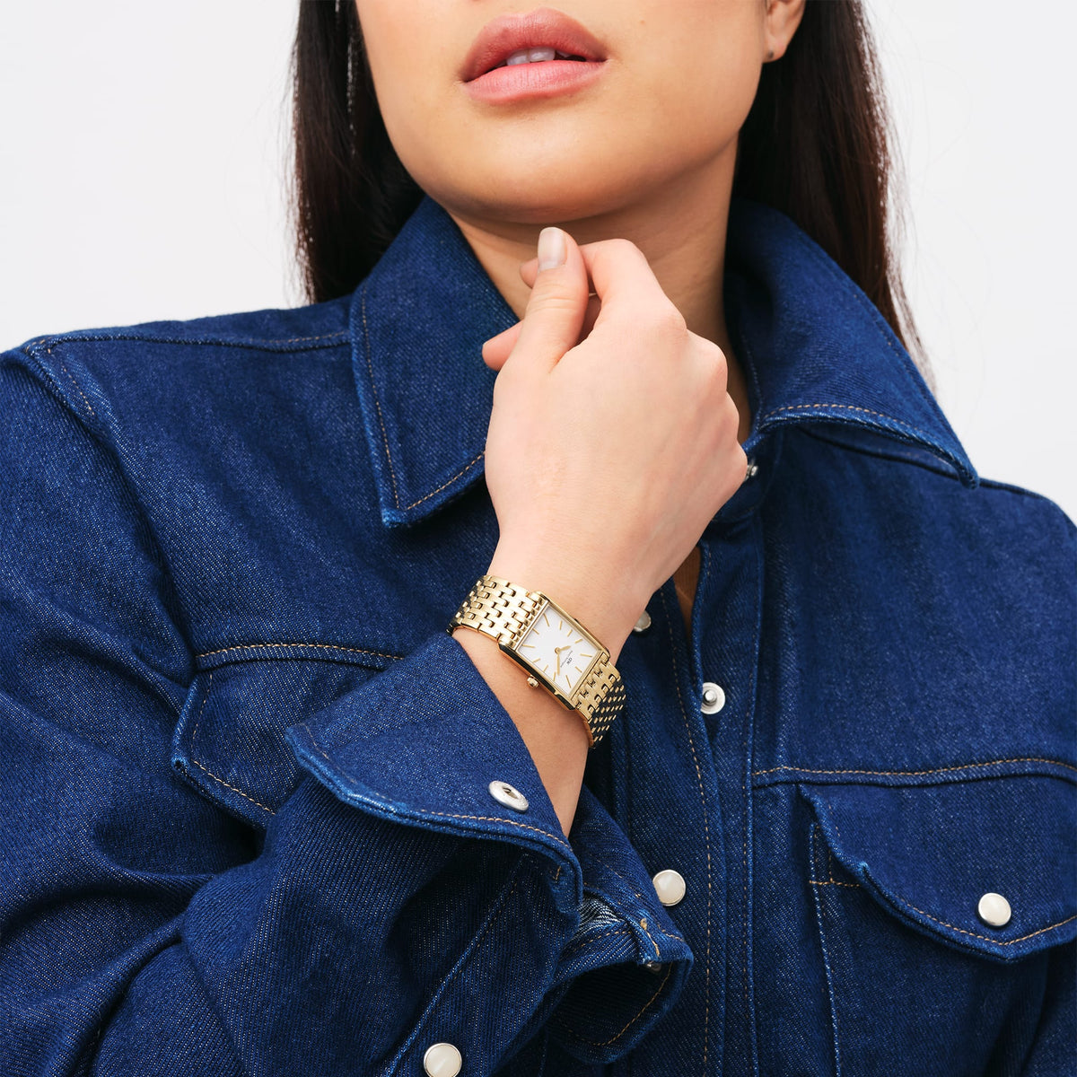 A woman is wearing the elegant Bound 9-Link Gold ladies' watch with a rectangular case and 9-link bracelet made of gold-coloured stainless steel, paired with a dark blue denim blouse.