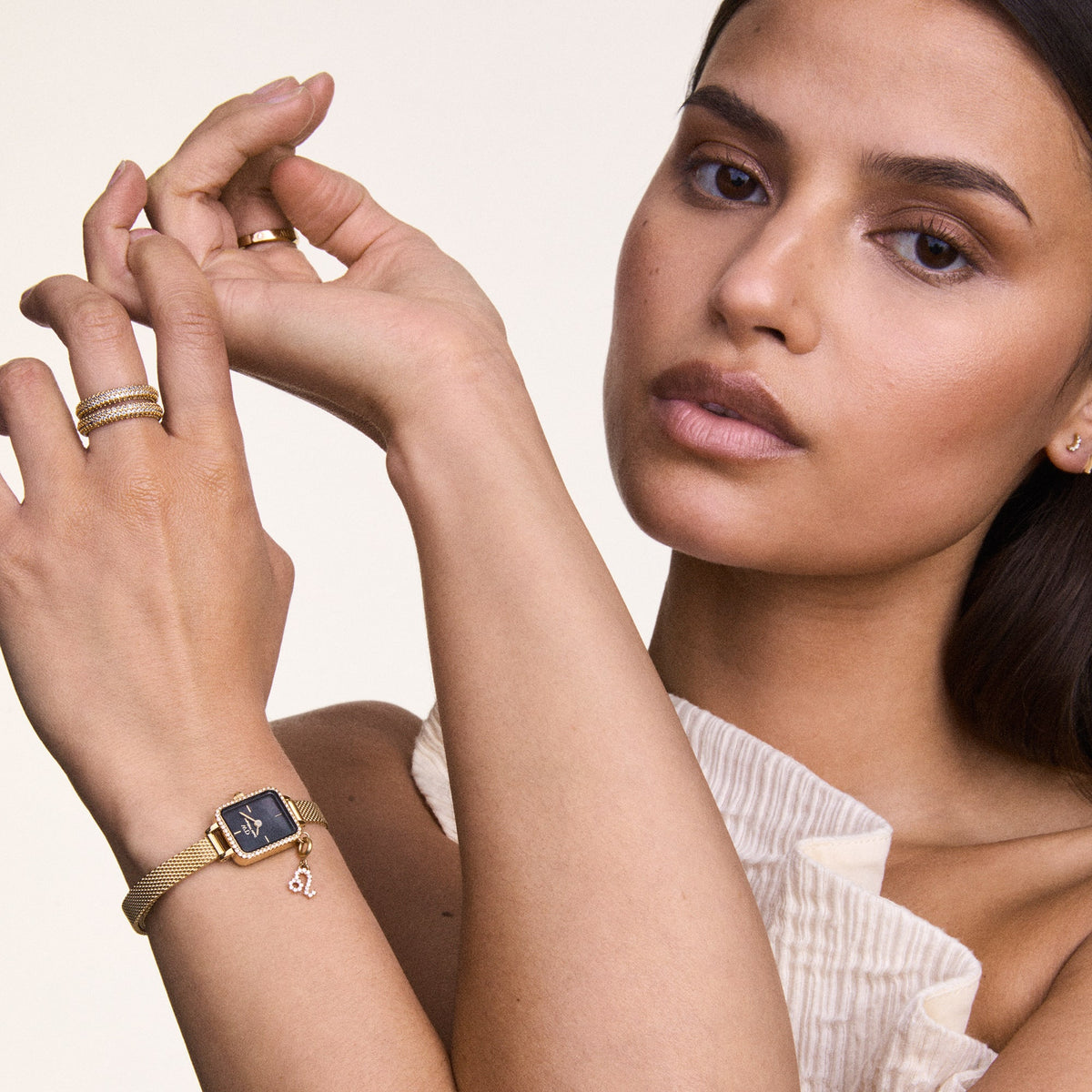 A woman is wearing the elegant Quadro Mini Crystal Zodiac Evergold women's watch with a rectangular case, black mother-of-pearl dial, gold-coloured mesh strap, and sparkling Zodiac charm on her wrist.
