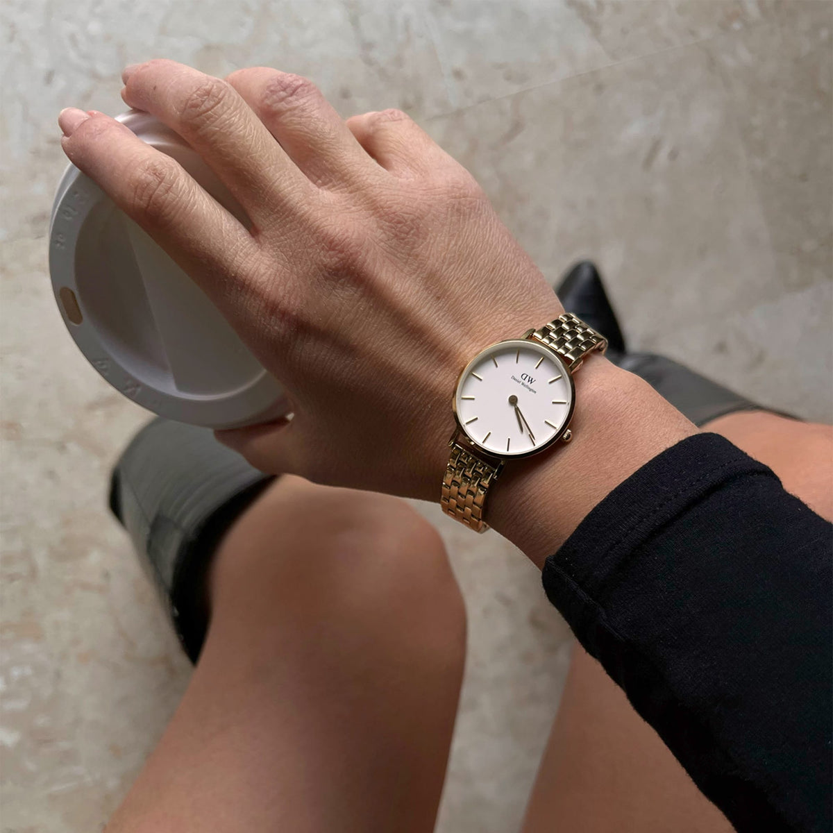 The gold Petite 5-Link Evergold women's watch with a white dial and 5-link bracelet is worn on the wrist while the person is holding a cup.