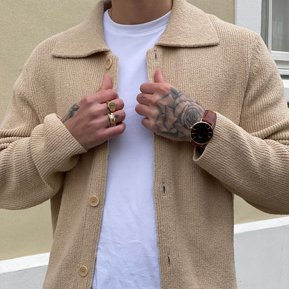 Hombre luciendo el reloj Classic St Mawes Amber Rose Gold con correa de piel marrón, combinado con chaqueta beige y anillos dorados en estilo casual elegante.