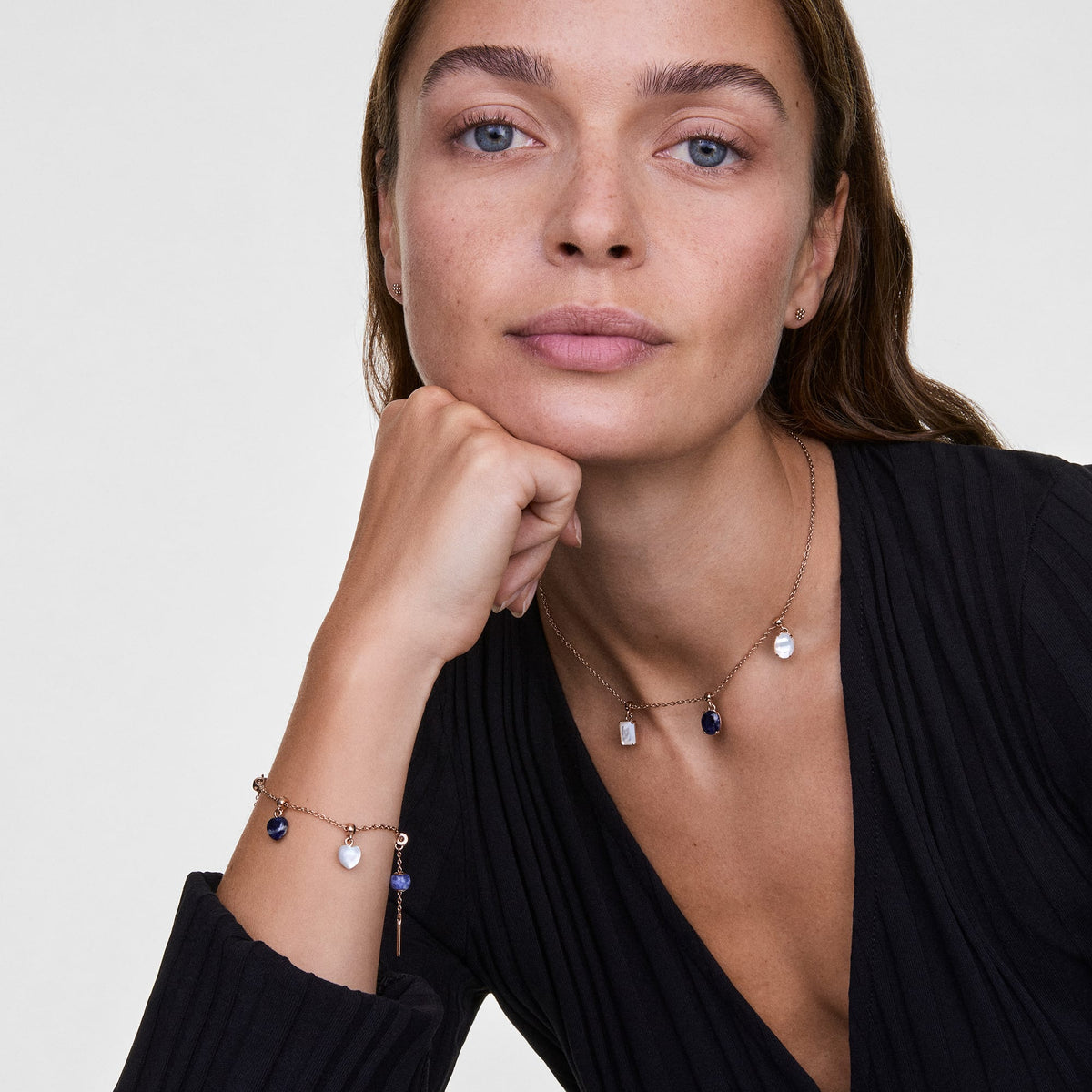 Mujer luciendo el charm Mother of Pearl Oval Rose Gold Charm en una pulsera y un collar de oro rosa combinados con otros charms de piedras semipreciosas, creando un estilo minimalista y elegante sobre un conjunto negro.