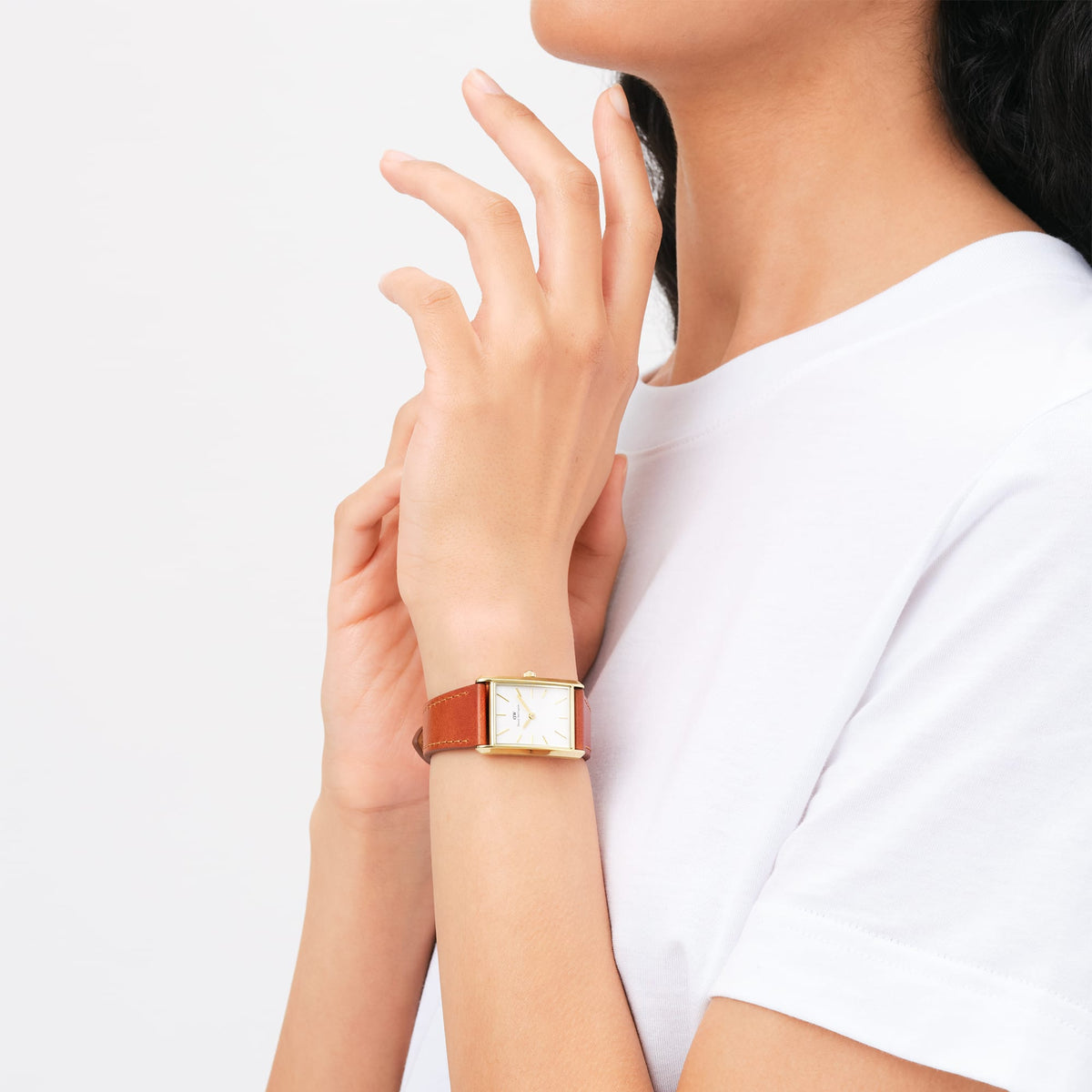 A woman stylishly wears the Bound Durham Gold ladies' watch with a rectangular gold-coloured case and light brown leather strap on her wrist with a white T-shirt.