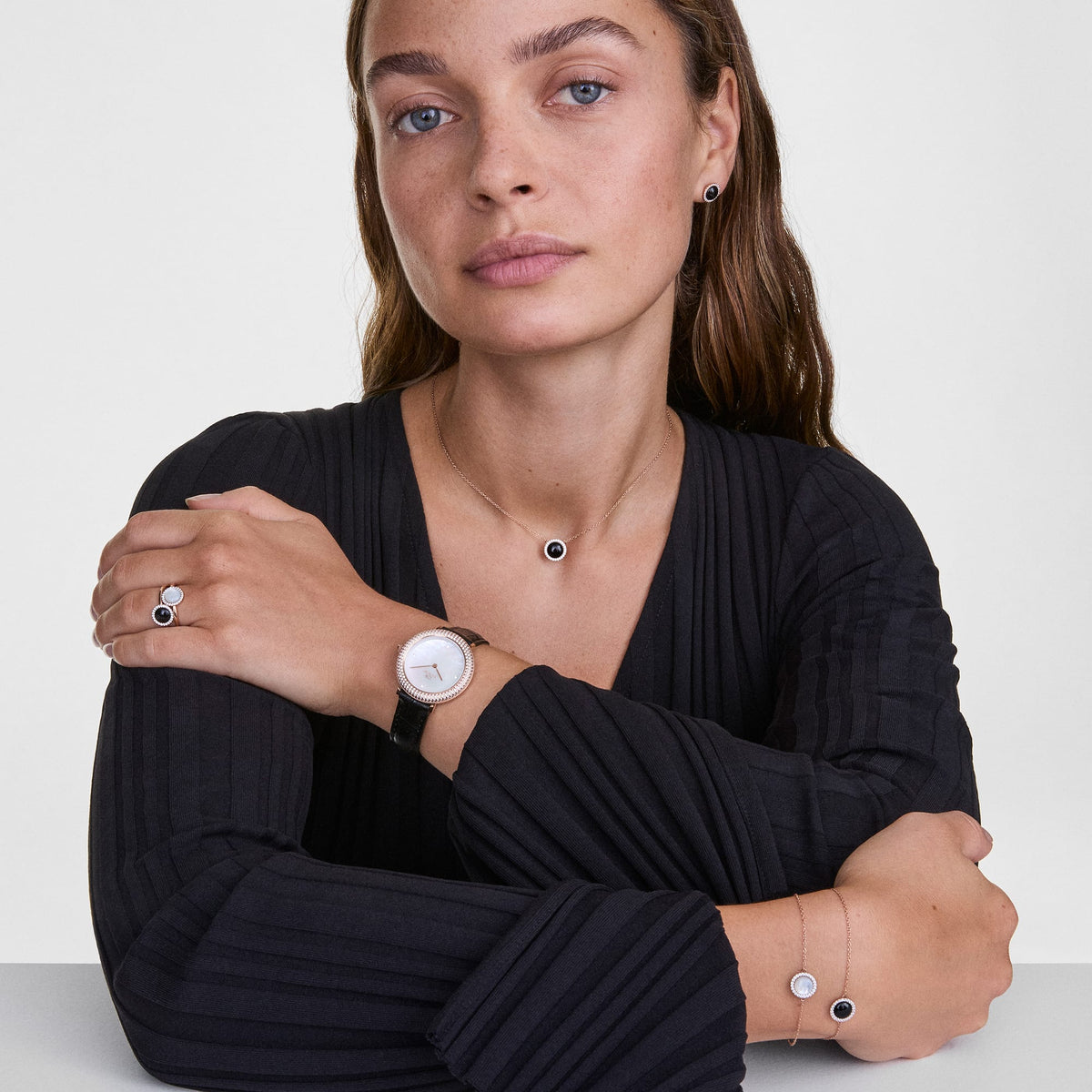 Mujer luciendo el collar Audrey con ágata negra y oro rosa combinado con pendientes, anillo, pulsera y reloj a juego sobre un conjunto negro