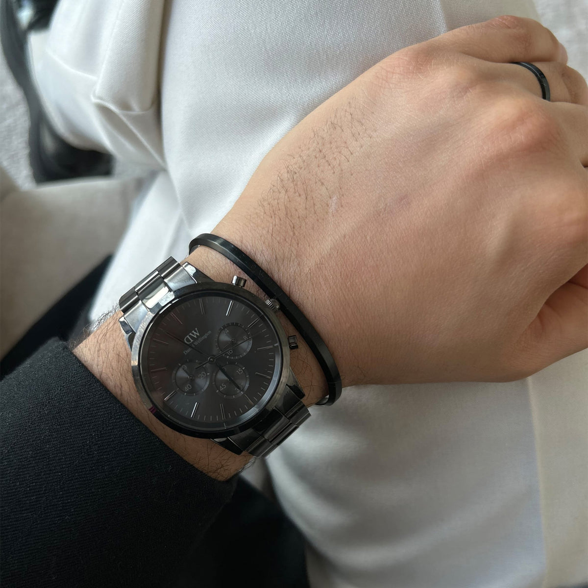 The Iconic Chronograph Link Onyx B is worn on the wrist and paired with a black bangle, complementing an elegant black and white outfit.