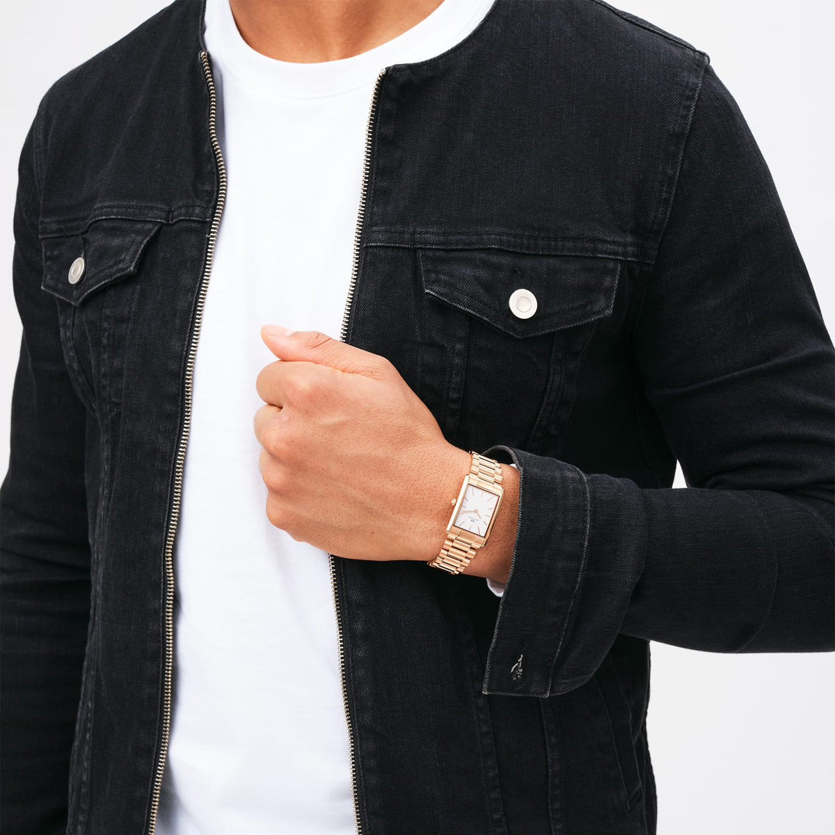 The Bound 3-Link Rose Gold watch by Daniel Wellington with a rectangular case and 3-link rose gold bracelet is worn on the wrist with a black denim jacket and white shirt.