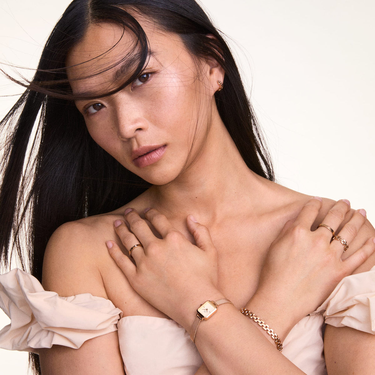 Woman wearing an off-shoulder top with the Quadro Mini Melrose Champagne women's watch in rose gold with a champagne-coloured dial and delicate mesh strap on her wrist, paired with subtle jewellery.