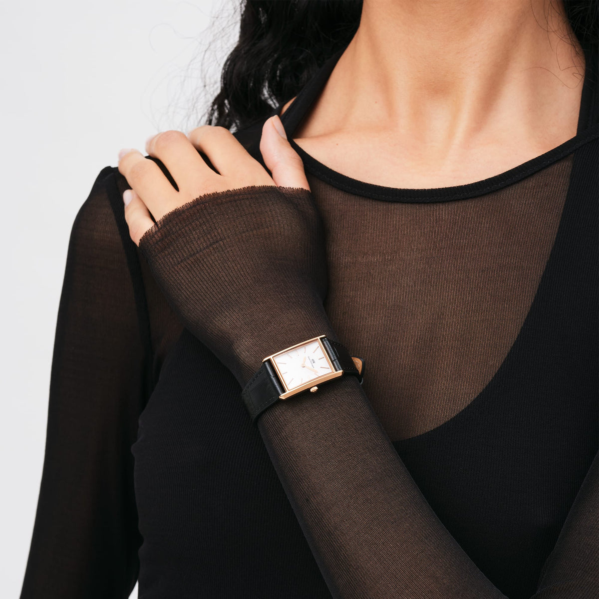 Elegant ladies' watch with a rectangular rose gold case and black crocodile-patterned leather strap, worn on the wrist with a black, sheer top.