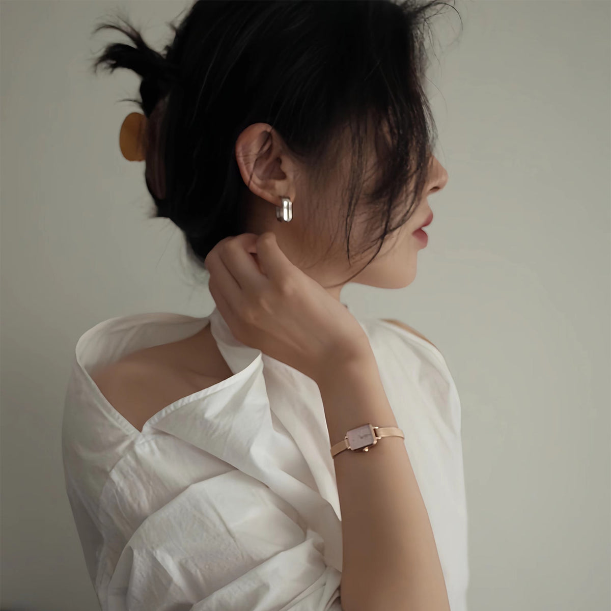 A woman wears the Quadro Mini Melrose Blush women's watch with a rectangular case and rose gold mesh strap on her wrist, paired with an elegant white blouse.