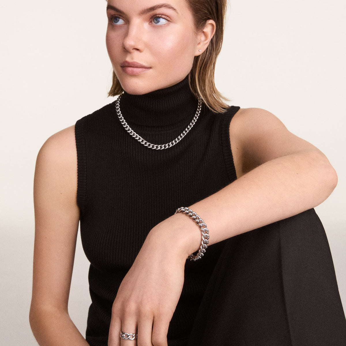 La modella indossa il bracciale *Chunky Chain* in acciaio argentato, abbinato a una collana dello stesso stile, su un outfit total black minimalista con dolcevita senza maniche.