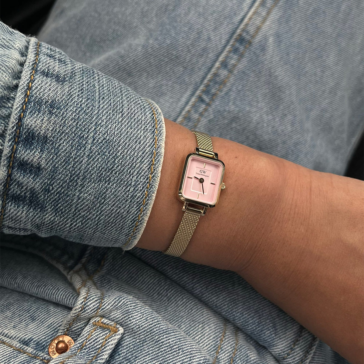 The Quadro Mini Evergold Blush women's watch with a rectangular gold-coloured case and rose-coloured dial is worn on the wrist with a denim jacket.