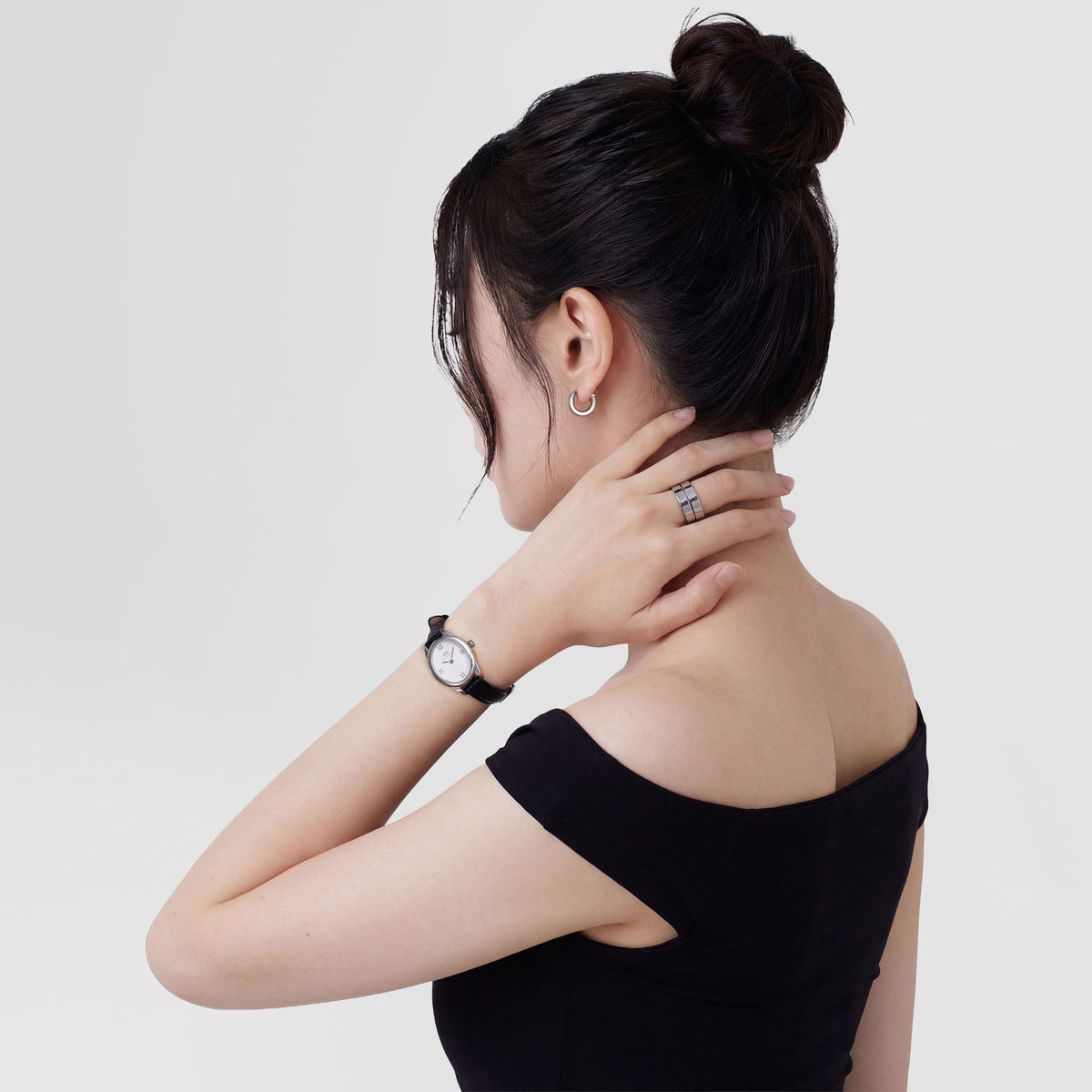 La modella, ritratta di profilo, indossa orecchini a cerchio in argento satinato da 3,5 mm, abbinati a un orologio e ad anelli. I capelli sono raccolti in uno chignon e il top è nero.