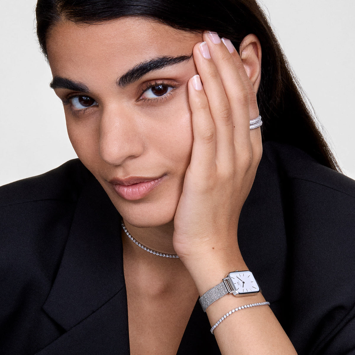 A woman wears the Classic Tennis Necklace Silver by Daniel Wellington as a sparkling silver necklace, paired with matching bracelet and watch, styled with an elegant black blazer.