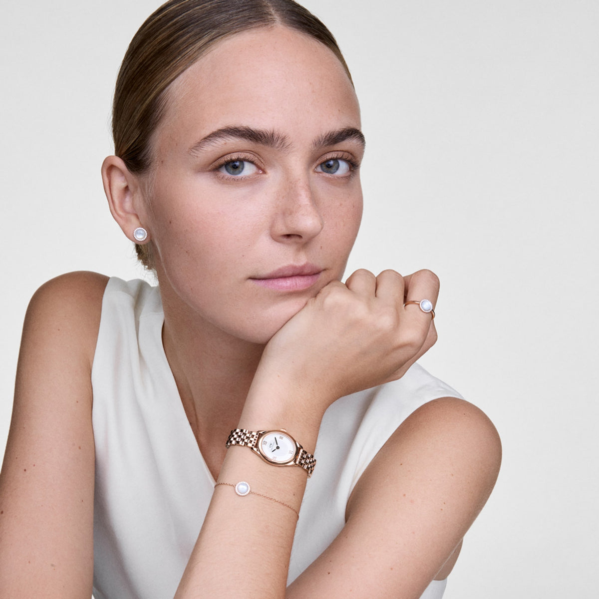 A woman wears the elegant Ophelia Mini ladies' watch in rose gold with an oval case and white dial on her wrist, paired with matching jewellery and a white top.