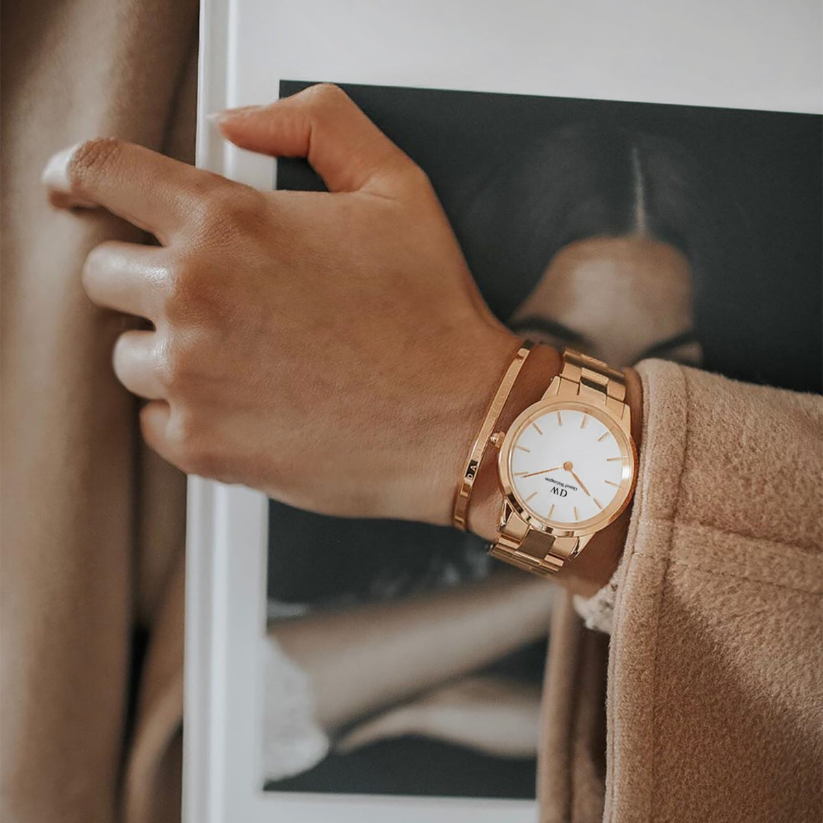 A woman wears the Daniel Wellington Iconic Link women's watch in rose gold with a white dial and matching bangle, paired with an elegant beige coat.