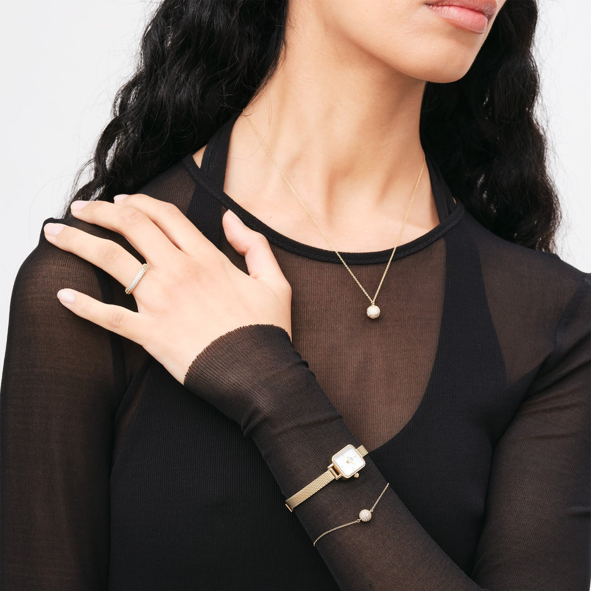 A woman wears the Quadro Mini Lumine Bezel Gold with a rectangular case, gold-coloured mesh strap, and crystal detailing on her wrist, paired with matching gold-coloured jewellery and an elegant black top.