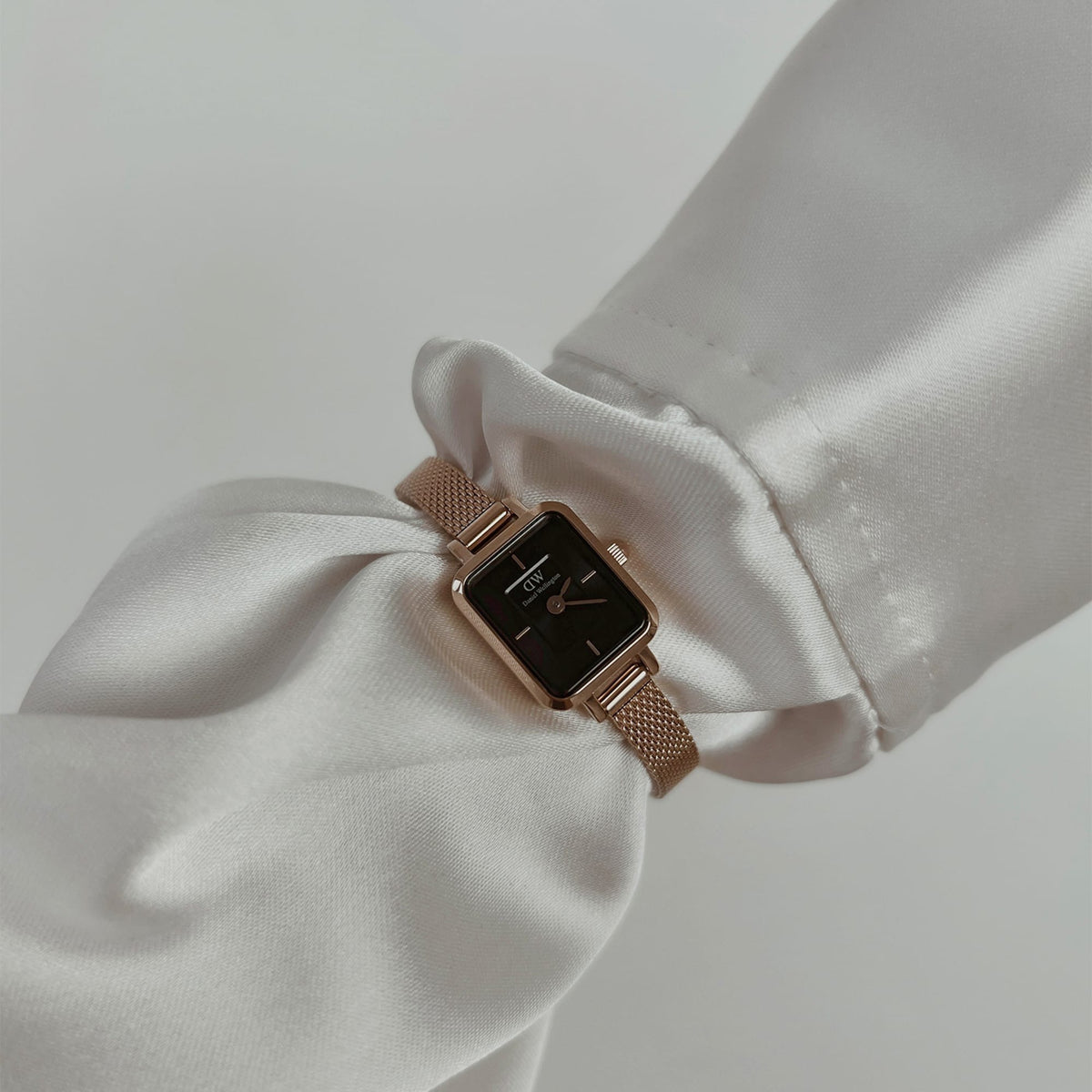 Elegant ladies' watch Quadro Mini Melrose Onyx with rectangular rose gold case and black dial on the wrist, worn with a white, silky blouse.