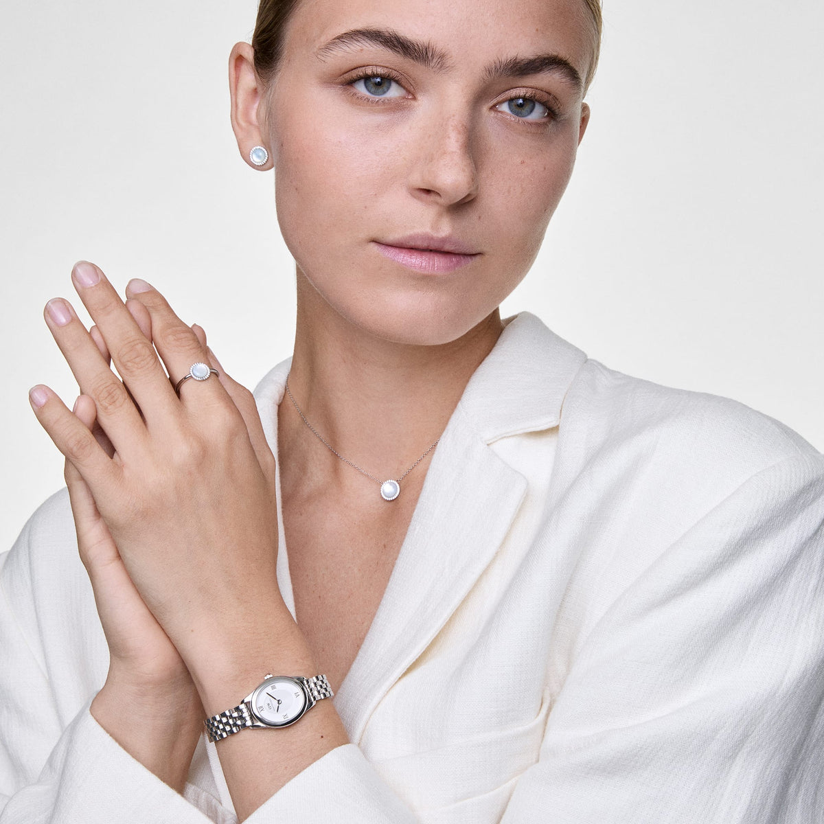 A woman wears the silver Audrey earrings with a shimmering mother-of-pearl stone and crystal accents, paired with a matching necklace, ring and watch for an elegant, coordinated look.