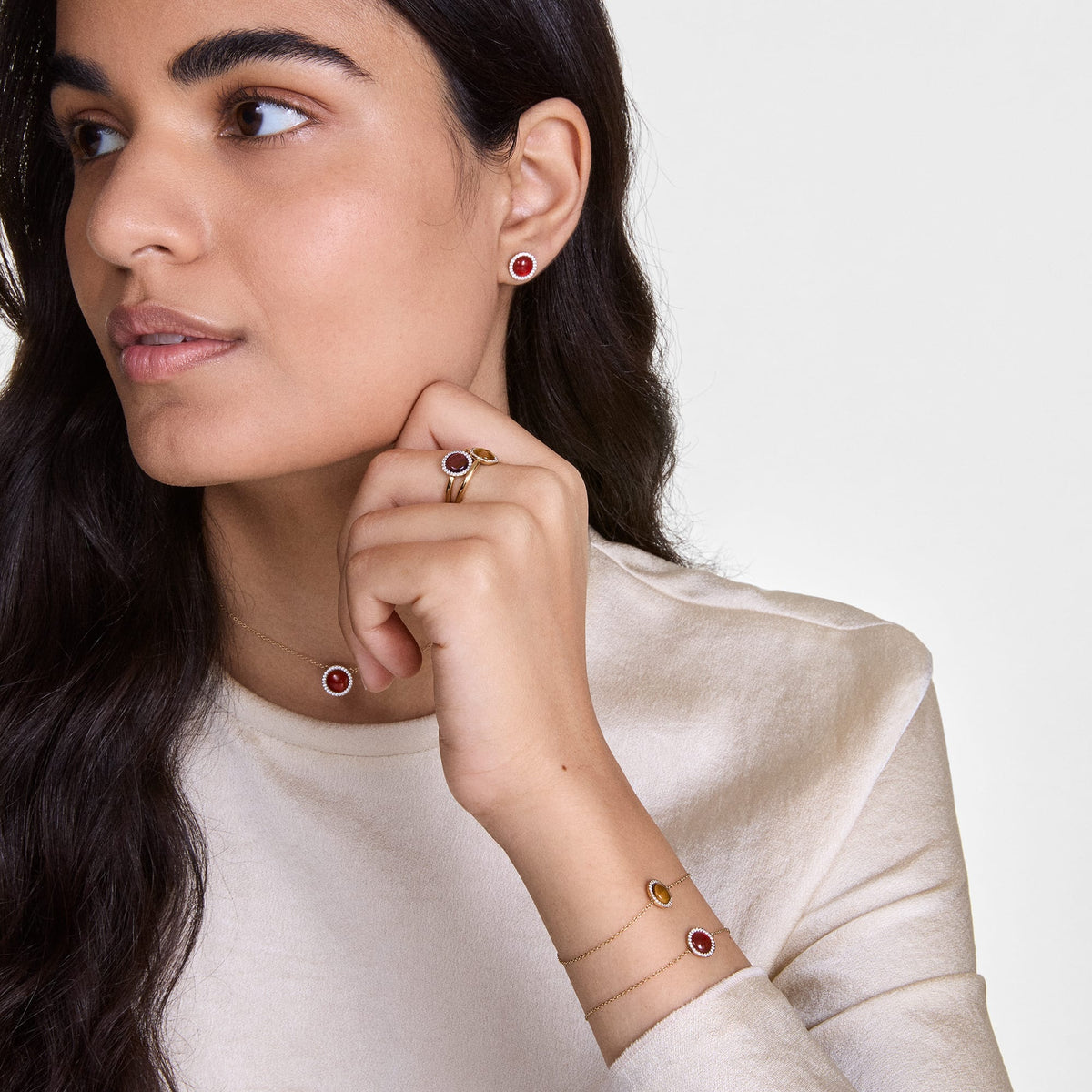 A woman wears elegant Audrey stud earrings in rose gold with red agate and white zirconia crystals, paired with a matching necklace, ring and bracelet.