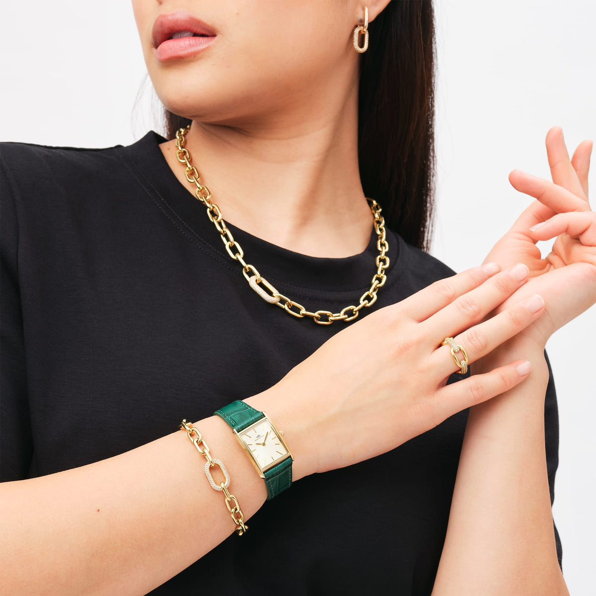 A woman is wearing a rectangular gold ladies' watch with a champagne-coloured dial and a green crocodile-embossed leather strap, paired with gold-toned jewellery.