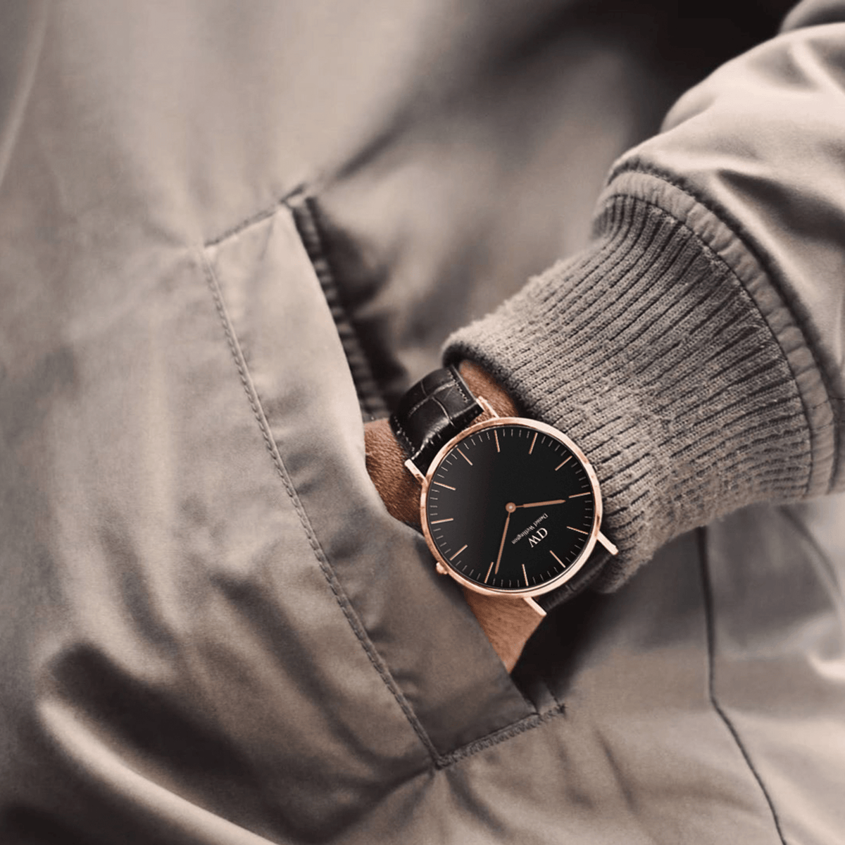 Hombre vistiendo el reloj Classic York Black Rose Gold en la muñeca con jersey gris y chaqueta, mostrando el diseño minimalista de la esfera negra y la caja de oro rosa.