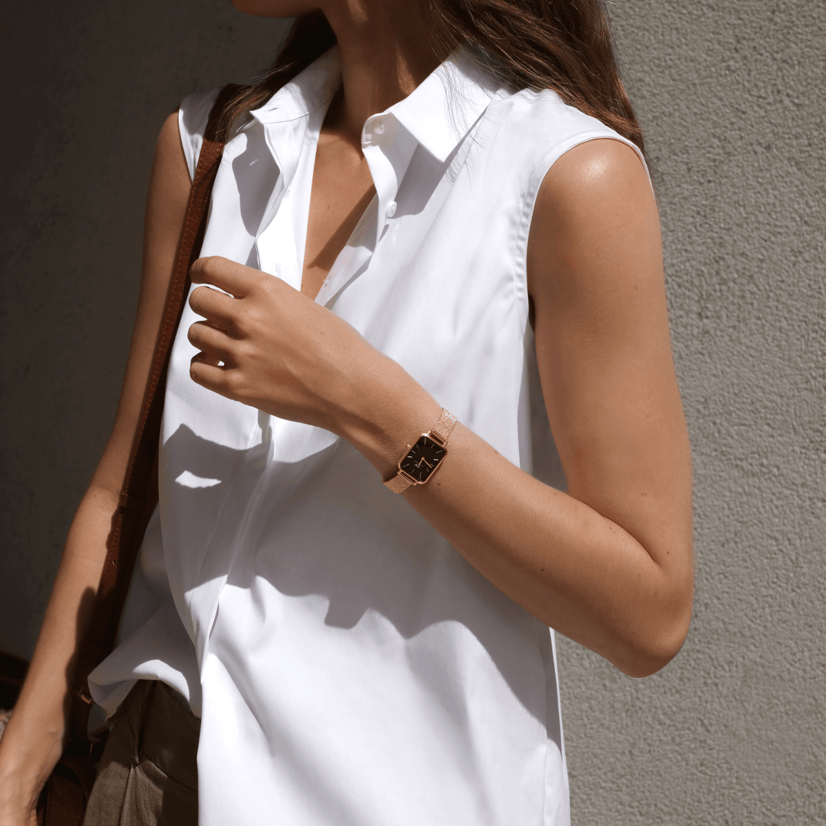 Woman wearing the Quadro Pressed Melrose women's watch in rose gold with black dial and mesh strap, paired with a sleeveless white shirt in sunlight.