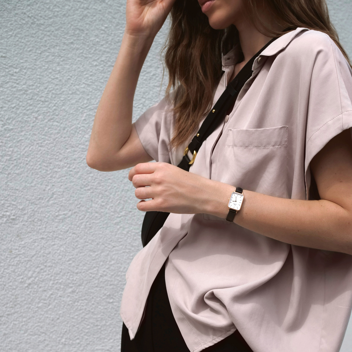 A woman wears the elegant Quadro Pressed Sheffield ladies' watch in rose gold with a rectangular case and black leather strap with a casual, light-coloured outfit.