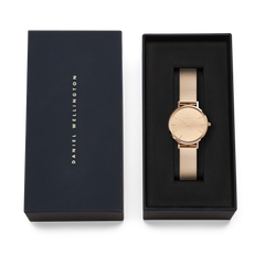 The Petite Reflection Rose Gold women's watch with a mirrored dial and mesh strap is presented in an elegant black Daniel Wellington gift box.