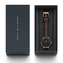 Orologio Petite York Black Rose Gold, incluso nella sua confezione regalo Daniel Wellington di colore antracite. Dotato di fibbia in oro rosa e cinturino in pelle marrone con texture effetto coccodrillo.