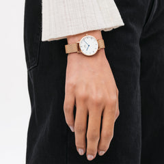 The Petite Roman Numerals Melrose women's watch in rose gold with a white dial and mesh strap is worn elegantly on the wrist.
