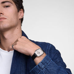 Man wearing an elegant Marlon Sheffield Linen Silver watch with a silver case, beige linen dial, and black leather strap paired with a denim jacket.