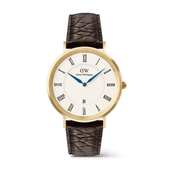 Orologio con numeri romani e datario, caratterizzato da una cassa dorata da 40 mm. Il quadrante bianco presenta numeri romani neri e lancette blu, abbinato a un cinturino in pelle marrone scuro con texture *Croc Belly*.