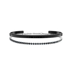 Set di bracciali in acciaio inossidabile, composto da un bracciale rigido nero con incisione *Daniel Wellington* e un bracciale tennis con zirconi cubici scuri su finitura argentata. Immagine su sfondo bianco.