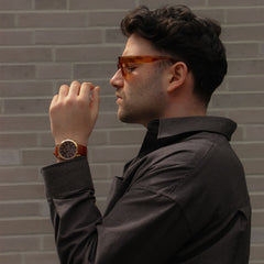 Hombre con gafas de sol ámbar lleva el reloj Iconic Chronograph St Mawes Amber RG en la muñeca, combinado con camisa oscura en un entorno urbano.