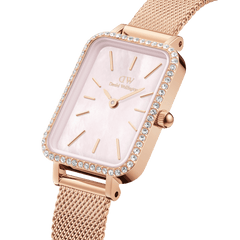 Close-up view of a rectangular ladies' watch in rose gold with a sparkling stone-set bezel, delicate pink mother-of-pearl dial, and fine mesh strap.