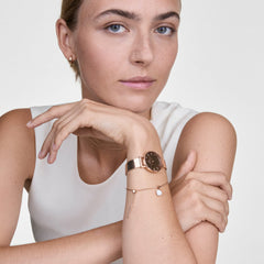 A woman wears the elegant Petite Reflection Rose Gold women's watch with a round mirrored dial and a fine rose gold mesh strap on her wrist, paired with delicate jewellery.