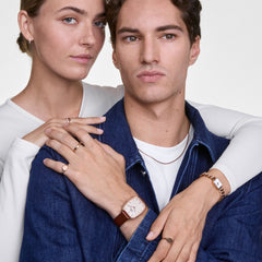 A man wears the Daniel Wellington Marlon St Mawes Linen Rose Gold with a cushion-shaped rose gold case, linen-coloured dial and brown leather strap on his wrist, paired with a casual outfit and jewellery.
