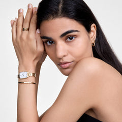 A woman wears the gold Quadro Roman Numerals 5-Link watch by Daniel Wellington on her wrist, paired with a gold-coloured bangle and ring for an elegant, modern look.