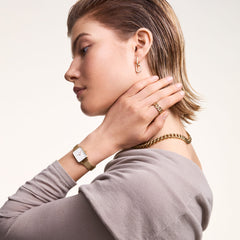 A woman wears the Quadro Pressed Evergold ladies' watch with a rectangular case and gold-coloured mesh strap on her wrist, paired with matching gold jewellery for an elegant, modern look.