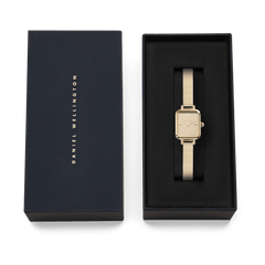The Quadro Mini Reflection Gold ladies' watch with rectangular case and gold-coloured mesh strap lies elegantly in a black Daniel Wellington gift box.